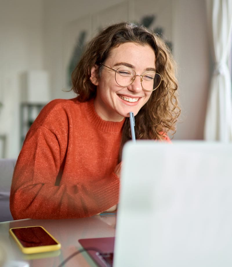 Young happy woman student using laptop watching webinar writing at home